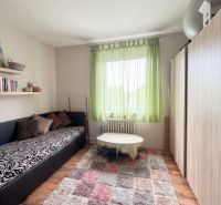 A room in a 3-room apartment with a sofa, shelves, a table, and a wooden decor floor.