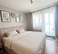 A bedroom in a three-room apartment with a wooden decor floor and balcony doors.