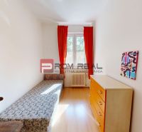 A room in a 4-room apartment with a bed, a dresser, and a window with red curtains.