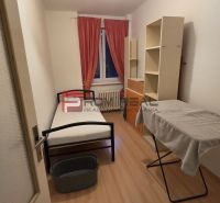 A simple room with a bed, an ironing board, and a floor with a wood pattern.
