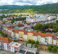 Púchov, Moyzesova Street: apartment buildings surrounded by greenery and commercial spaces in the background of nature.