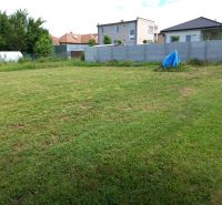 A grassy plot for living in Beladice, surrounded by a fence and family houses.