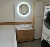 Bathroom in a 2-room apartment with a bathtub, washing machine, and wooden decor flooring.
