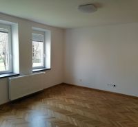 A spacious room with wooden decor flooring and large windows in a 2-room apartment.