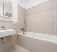 A bathroom with a bathtub and a sink in a two-room apartment. Neutral tiles on the walls.