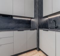 Dark gray kitchen unit with matte cabinets and a wooden decor floor in a 2-room apartment.