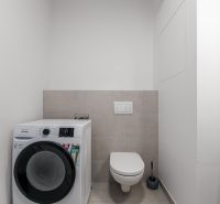 Bathroom with a washing machine and toilet in a 2-room apartment, light neutral wall colors.