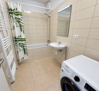 Bathroom with a shower curtain, washing machine, and sink in a 2-room apartment.