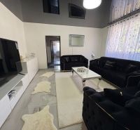 A living room in a family house with white furniture, a black sofa, and decorative rugs.