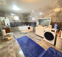 A family house bathroom with a bathtub, toilet, and washing machine on a floor with a wooden decor.