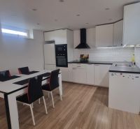 A kitchen in a 2-room apartment with white furniture, a dining table, and a floor with a wooden decor.