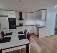 A kitchen in a 2-room apartment with a wooden decor floor and white furniture.