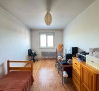 A room in a 3-room apartment with a wooden decor floor, simple furnishings, and a work corner.
