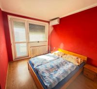 A bedroom with red walls, a wooden bed, and a floor with a wooden decor in a 3-room apartment.