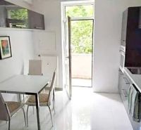 The kitchen of a two-room apartment with white tiles and a dining table by the window.