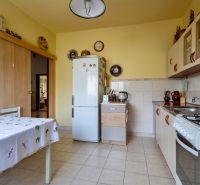 A kitchen in a family house with tiles, a refrigerator, and a table with a tablecloth.
