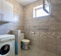 A bathroom in a family house with a washing machine, toilet, and tiles in neutral colors.