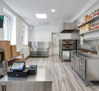 Kitchen commercial space with stainless steel equipment, storage, and a cash register system on a wooden decor floor.