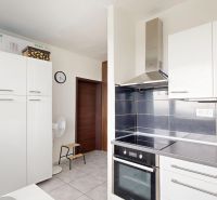 A kitchen with white cabinets, a range hood, and ceramic tiles in a studio apartment.
