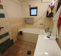 A bathroom in a family house with a bathtub, a washing machine, and tiles in vibrant colors.