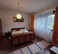 A bedroom in a family house with antique furniture, curtains, and a large window.