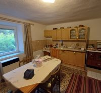 A kitchen in a family house with wooden cabinets, a large window, and a carpet on the floor.