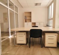 Offices with a large desk, a folding chair, and a simple shelf on the floor with a wooden decor.