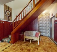Interior of a family house with a wooden staircase, carpet, and wicker furniture.