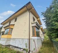 A family house in Veličná surrounded by trees and grass under a blue sky.
