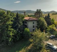 A building surrounded by trees and cars in the picturesque landscape of Slatinské Lazovček with development plots.