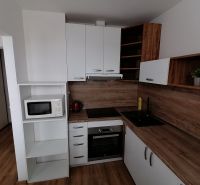 A kitchen with white cabinets and appliances in a studio apartment; floor with wood decor.