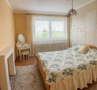 Bedroom in a family house with a wooden decor floor, floral bedspread, and a vanity table.