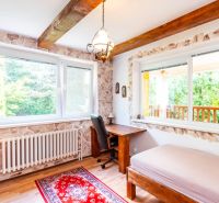 A room with a desk, wooden floor decor, and large windows in a family house.