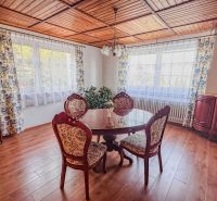 A dining room with a wooden ceiling, a floor with a wooden decor, and antique furniture.