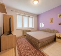 A bedroom in a family house with a purple wall, carpet, bed, television, wooden decor flooring.