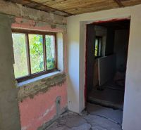 The interior of a cottage with peeling plaster and a view of the garden through the window.