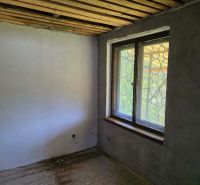 The room in the cottage has a concrete floor and a simple window with a grille.