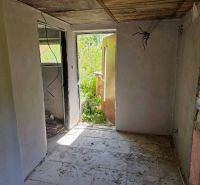 The interior of a cottage with white walls and an unfinished ceiling, entrance to the garden.