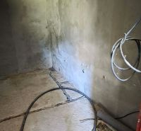 Gray walls in a cabin with a concrete floor and cables on the floor.