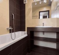 A bathroom in a 3-room apartment with a bathtub, a sink, and dark tiles.
