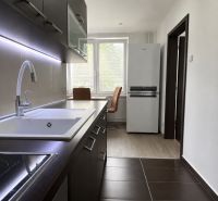 A kitchen in a 3-room apartment with a wooden decor floor, dark cabinets, and a white sink.