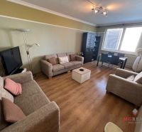 Living room with wood-patterned flooring, sofas, and a coffee table in a three-room apartment.
