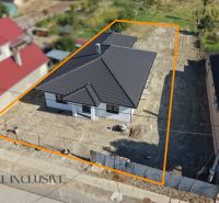 A family house in Tomášikovo with a dark roof and a fenced plot of land with planting.