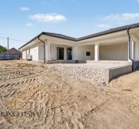 A family house in Tomášikovo with a terrace and an uneven plot under the blue sky.