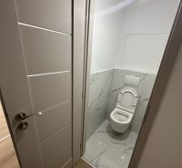 A toilet with white tiles and doors, and a floor with a wooden design.