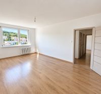 An empty room with a wooden floor, large windows, and white walls.