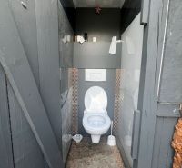A toilet in a cabin, gray walls, decorative cladding, floor with wooden decor.