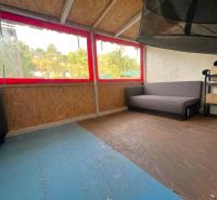 The attic of the cottage with windows and a wooden decor floor, a sofa, and shelves.