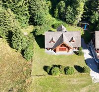 A cottage in Banská Bystrica surrounded by a dense forest and green lawn.
