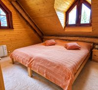 Attic bedroom in a cottage with a bed, wooden walls, and a carpet.